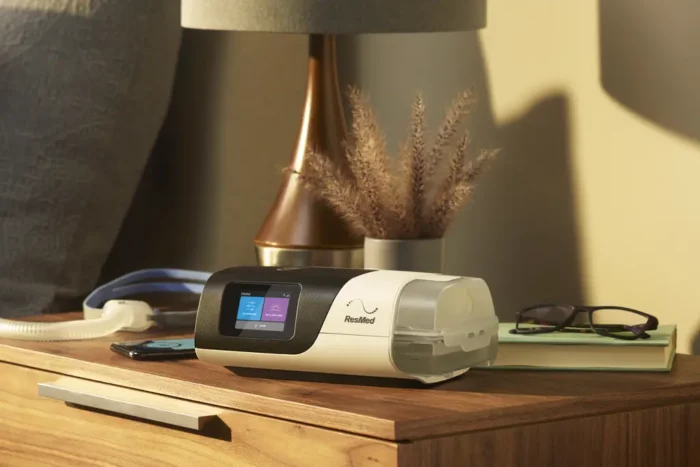 An electronic device, ResMed AirSense 11 Autoset APAP Machine with HumidAir Humidifier and Heated Tubing, is sitting on a nightstand.