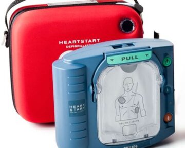 A Philips HeartStart OnSite AED defibrillator next to a red bag.