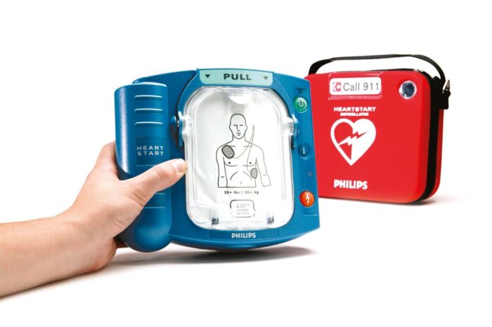 A hand grasping a Philips HeartStart OnSite AED.