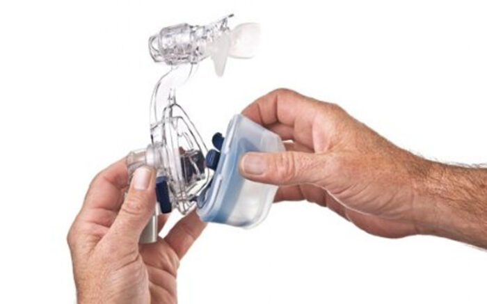 Two hands hold parts of a transparent ResMed Mirage SoftGel Nasal CPAP Mask Cushion & Clip, one grasping the mask and the other securing the cushion attachment.