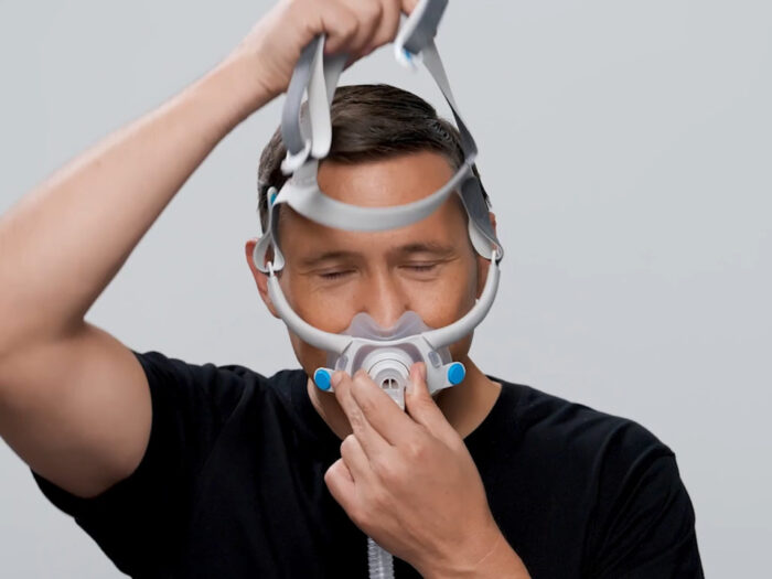 A person in a black shirt adjusts their ResMed AirFit F40 Full Face CPAP Mask against a plain background.