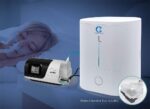 A woman sleeps with a nasal mask connected to a CPAP machine featuring the CSpring MK3 Automatic CPAP Water Chamber Replenishing System, while an oxygen concentrator sits on her bedside table.