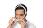 Man wearing a ResMed AirTouch N30i Nasal CPAP Mask (Fit Pack), adjusting the nose section, against a white background.