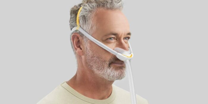 Middle-aged man wearing a Fisher & Paykel Solo Nasal CPAP Mask (Fit Pack) with headgear, viewed from the side, on a light gray background.