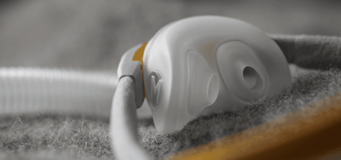 Close-up of a Fisher & Paykel Solo Nasal Pillow CPAP Mask (Fit Pack) with tubing, resting on a textured gray fabric surface.
