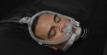 A person sleeps wearing the ResMed AirFit X30i Full Face CPAP Mask, with illustrated sound waves by the nose.