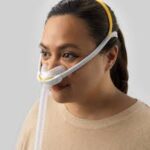 Woman wearing the Fisher & Paykel Solo Nasal CPAP Mask (Fit Pack) with head straps and a connected breathing tube.