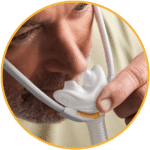 Close-up of a man fitting the Fisher & Paykel Solo Nasal Pillow CPAP Mask (Fit Pack) over his nose, holding the mask with one hand.