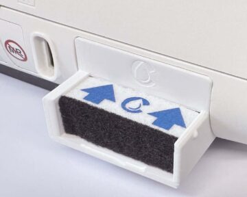 Close-up of a removable air filter cartridge with blue arrows on a white appliance.