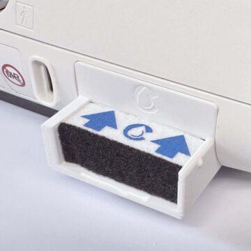 Close-up of a removable air filter cartridge with blue arrows on a white appliance.