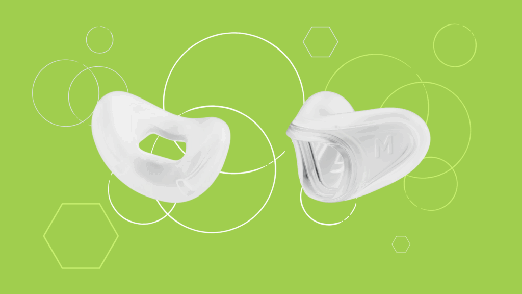 Two white silicone nose pieces from the Fisher & Paykel Solo Nasal Mask rest on a green background with white circles and hexagons.