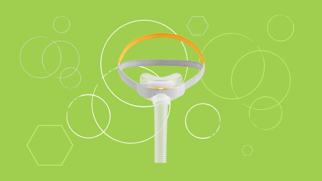 A Fisher & Paykel Solo Nasal Pillow Mask with head straps is displayed on a green background with white circles and hexagons.