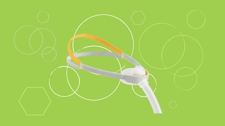 White and orange Fisher & Paykel Solo Nasal Pillow Mask CPAP headgear with hose on a green background featuring circles and hexagons—perfect for a detailed product review.