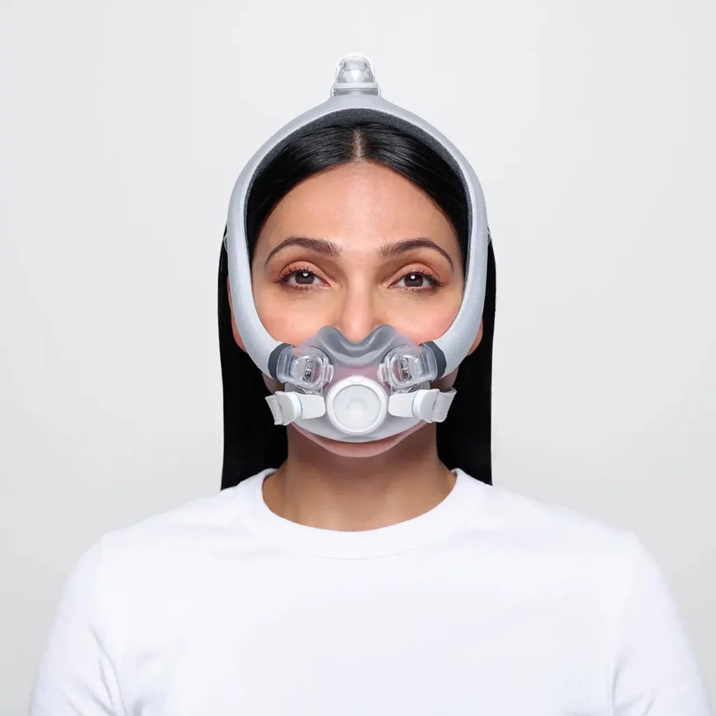 Woman wearing a ResMed AirTouch F30i Comfort Full Face CPAP Mask with headgear, posing against a plain white background.