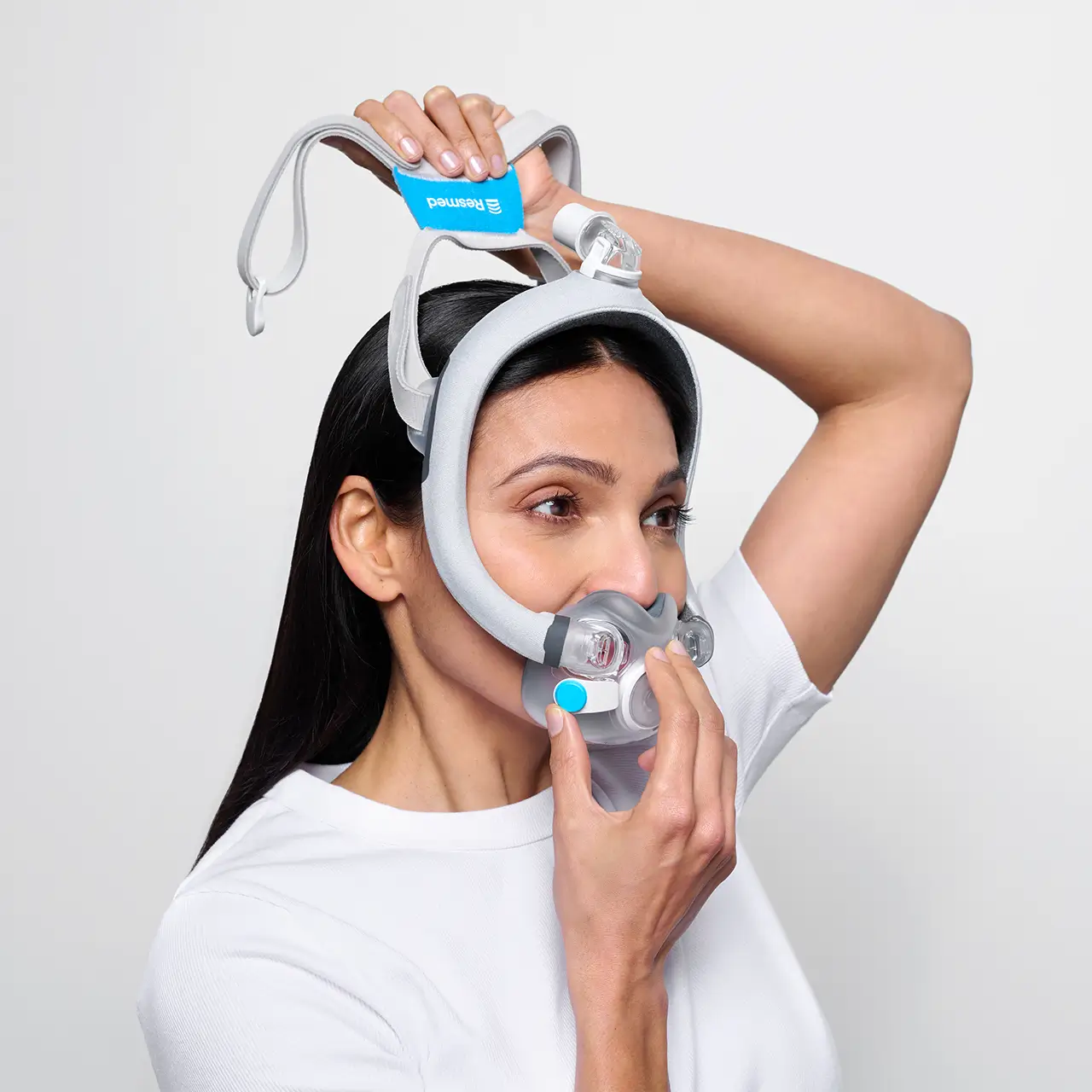 A woman adjusts the top strap for comfort as she fits the ResMed AirTouch F30i Comfort Full Face CPAP Mask securely over her nose and mouth.