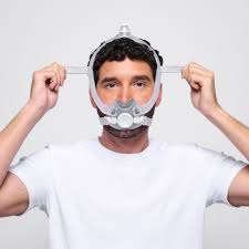 A man in a white shirt, facing forward against a plain background, puts on the ResMed AirTouch F30i Comfort Full Face CPAP Mask, showcasing its comfort and ease of use.